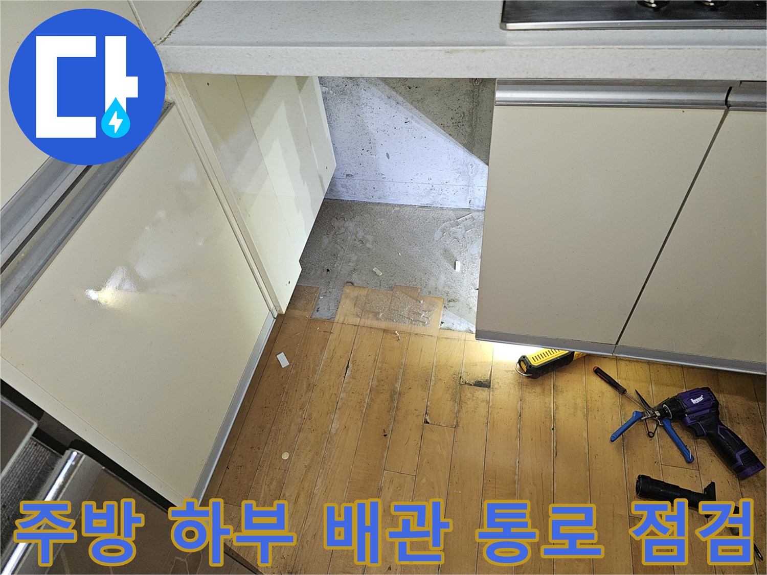 싱크대 아래 노출된 바닥 공간과 작업용 펜치 및 전등