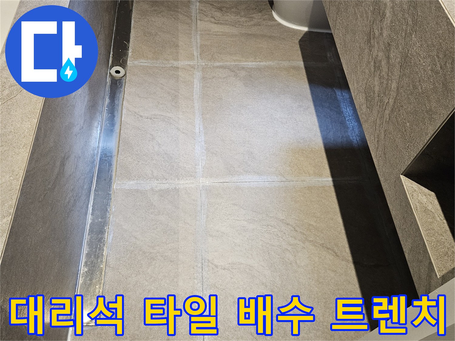 욕실 바닥의 대리석 타일과 금속 소재의 배수 트렌치 모습