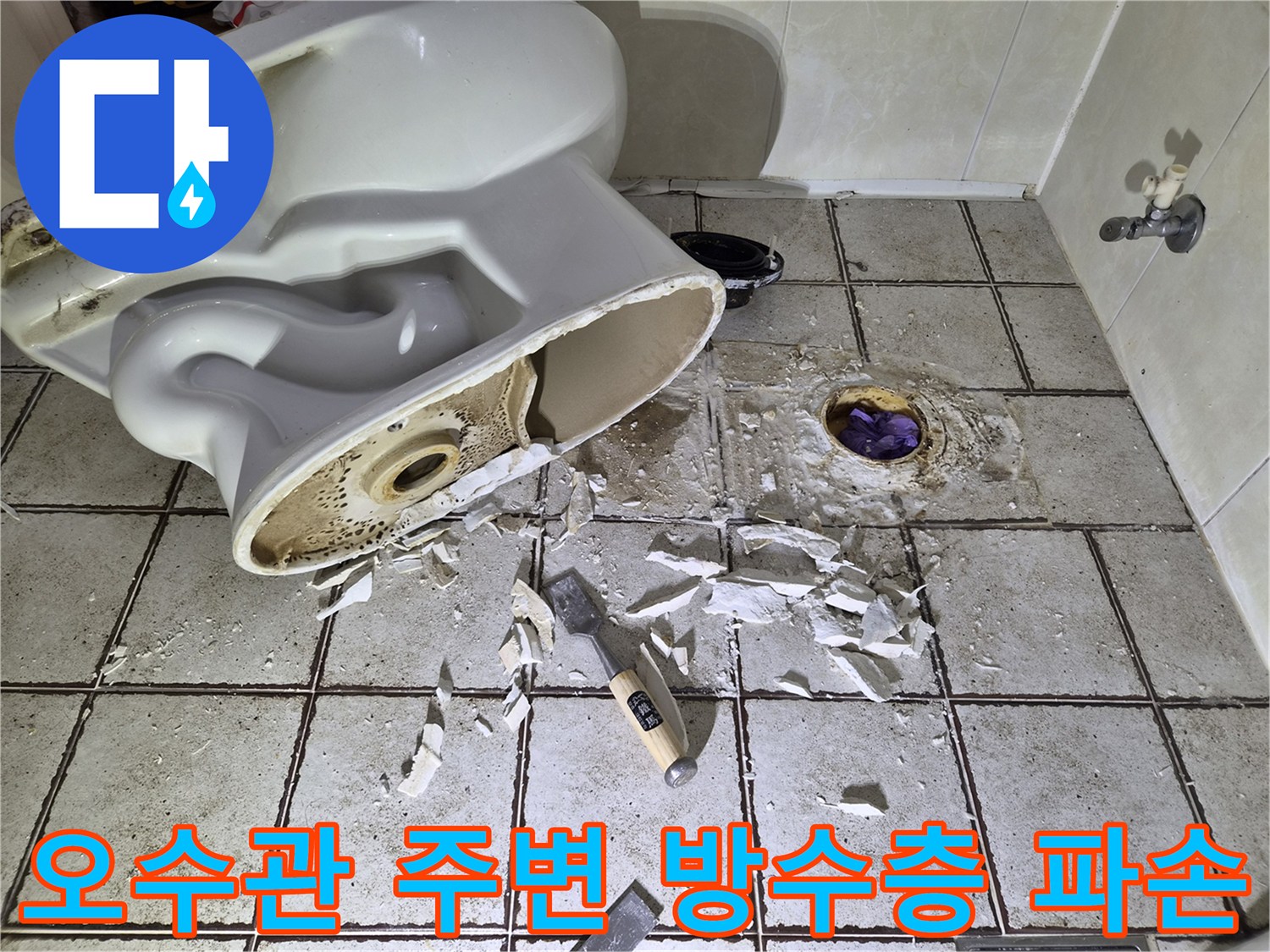 변기 배관 주위의 깨진 타일과 노출된 오수관 부위를 촬영한 모습입니다.